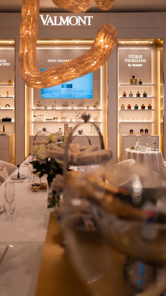 Eine geschwungene goldfarbene Leuchte hängt über der gedeckten Tafel; dahinter stehen Produkte in beleuchteten Valmont-Regalen.